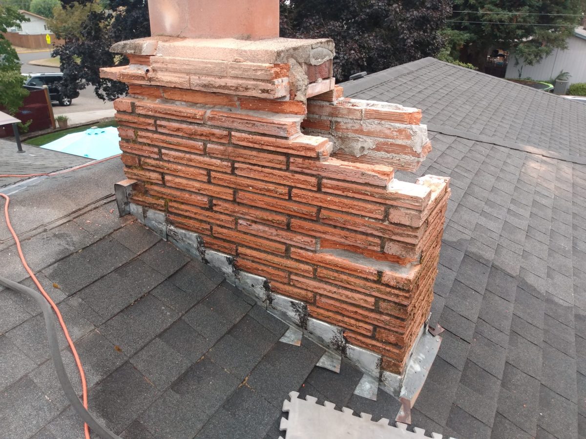 Damaged brick chimney on residential roof.