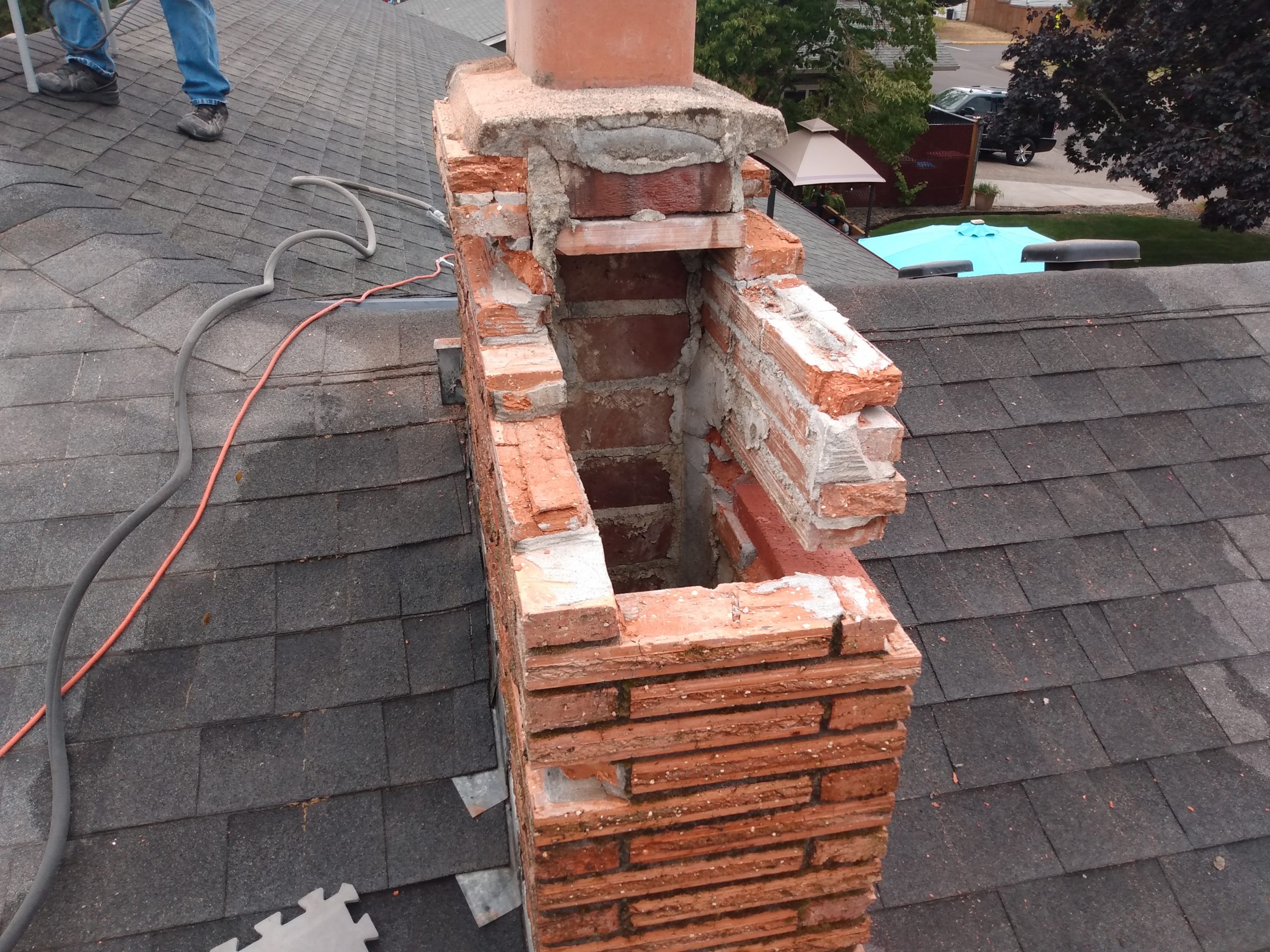 Damaged brick chimney on residential roof.