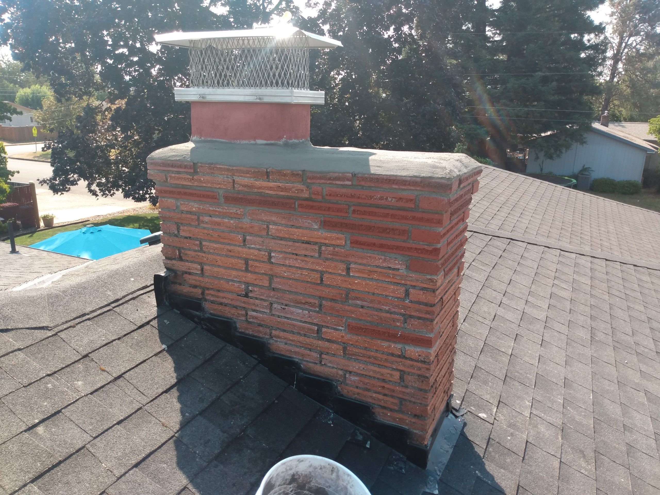 Brick chimney on residential rooftop with pool background.