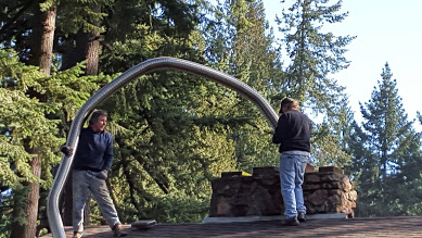 Two people by metal sculpture in forest clearing.