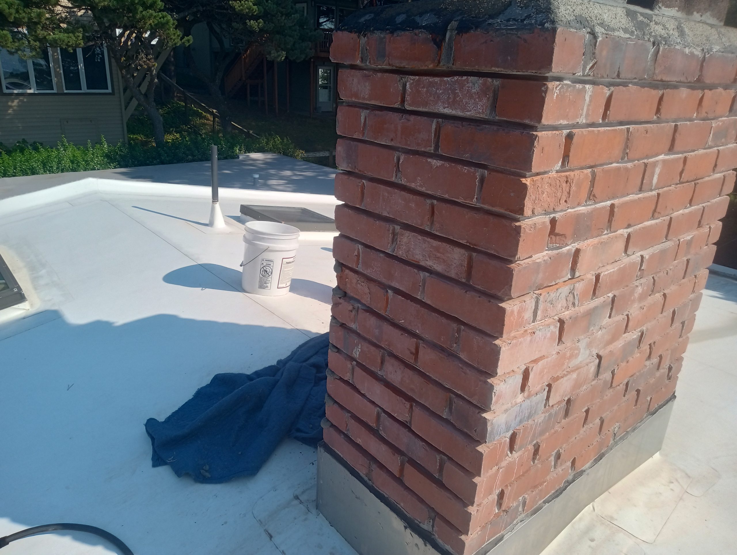 Newport Oregon 2 sides of chimney prepared for mortar joint repair Brick chimney on flat white roof with objects. Newport Oregon home. Mortar joints have been ground out in preparation for repairs.